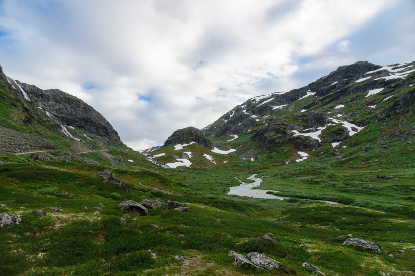 Fotografi av et dalføre i fjellandskap med grønt gress og noen flekker med snø.